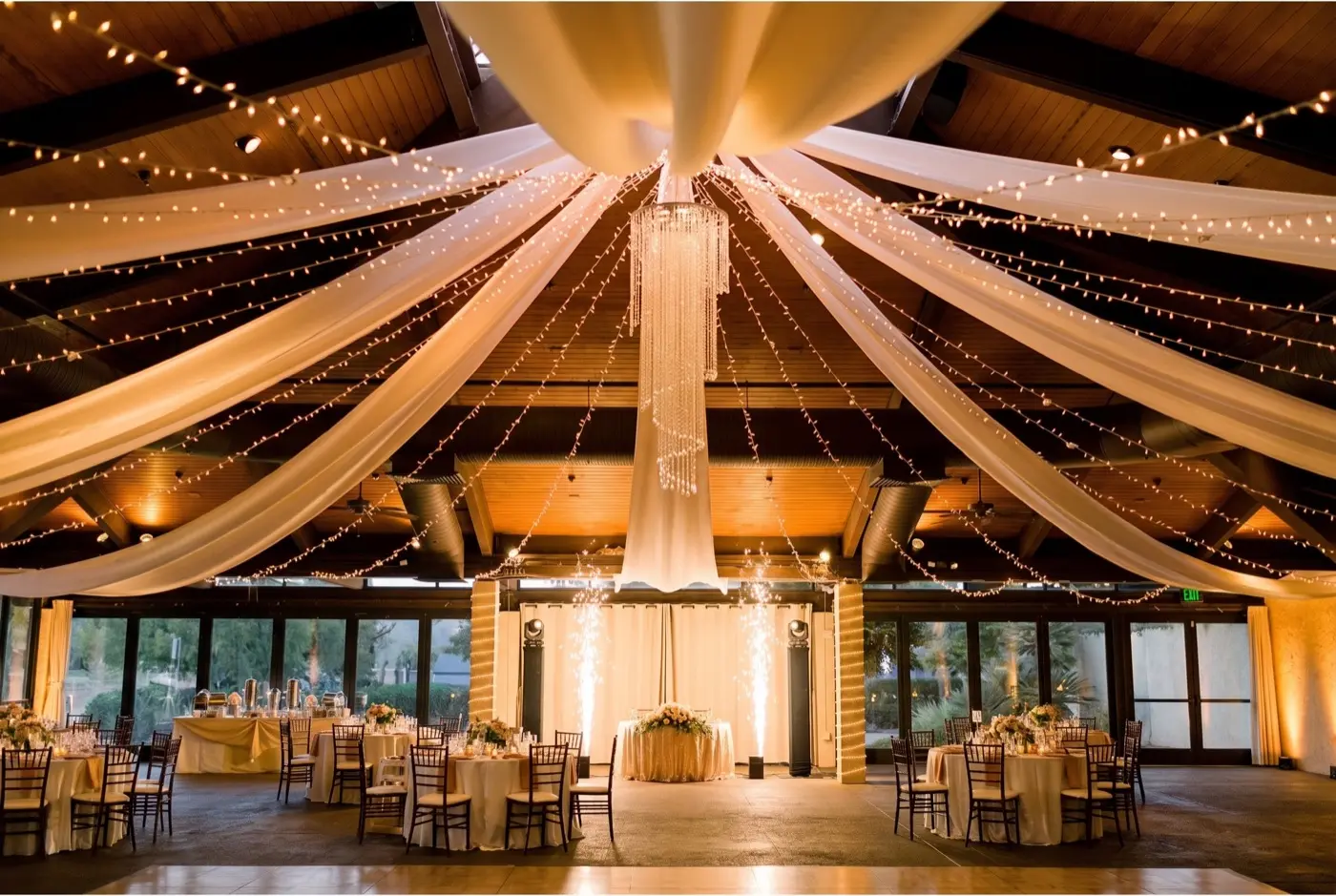 The same pavilion at night in warm champagne and amber light with cold sparks behind the head table